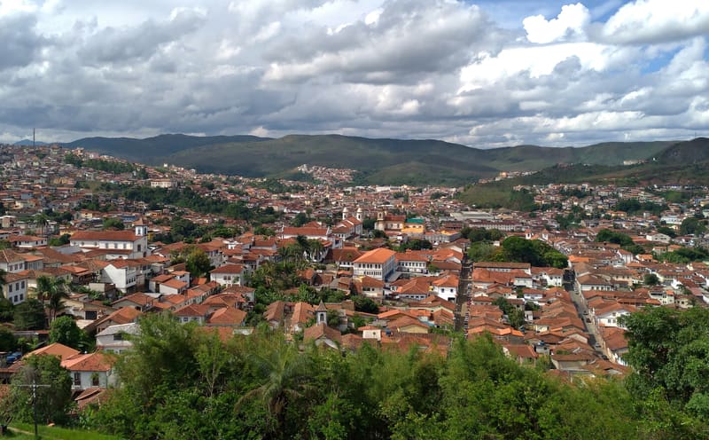 Vista panorâmica do centro histórico de Mariana, com telhados de telha, torres de igrejas e as montanhas de Minas ao fundo